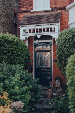 Londra, İngiltere - 22 Nisan 2020: Londra 'da bir Edwardian evinin lekesiz ahşap ön kapısı, seçici odak, ağaçlar çerçeveli. Edwardian evleri basit tasarımı destekliyor ve el yapımı ürünleri takdir ediyor..