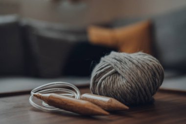 Çağdaş Scandi iç mekanında, ahşap bir masa üzerinde gri bir yün yumağı ve büyük dairesel örgü iğneleri, sığ bir odak yakın.