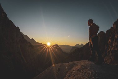 Hiker watching the beautiful sunset in a scenic mountain range clipart