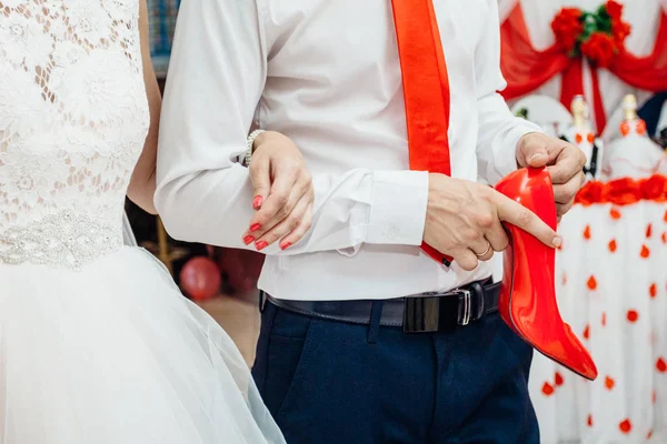Zapato de novia rojo en las manos de su marido — Foto de Stock