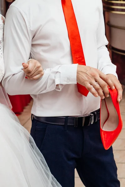El novio sostiene el zapato rojo de la novia. — Foto de Stock