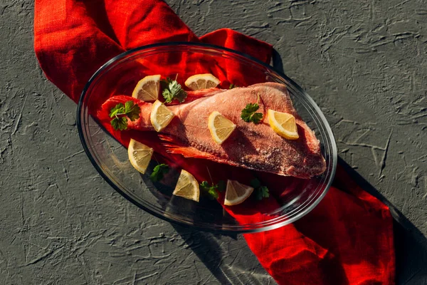 Baharatlı, limonlu, tuzlu ve maydanozlu bir kabın içinde kırmızı levrek. Yakın çekim, üst görünüm