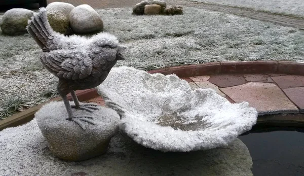 Decorative figurines (bird on stone) in the garden near the pond under the first fallen snow.