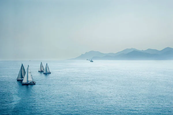 Sailing regatta or a group of small water racing boats and helicopter in the Mediterranean, a panoramic view with blue mountains on a horizon