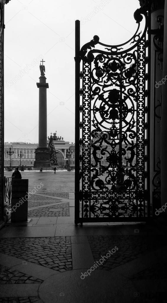 View of the Palace Square and the Alexandrian Column with an Angel through an open cast-iron gate, St. Petersburg, Russia. Black and white photography.