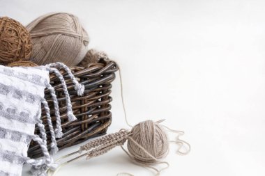 Hasır sepetin içinde örgü iğneleri, iplik gri ve kahverengi yün yumakları, açık arkaplanda. Hobi, el işi ve konfor kavramı