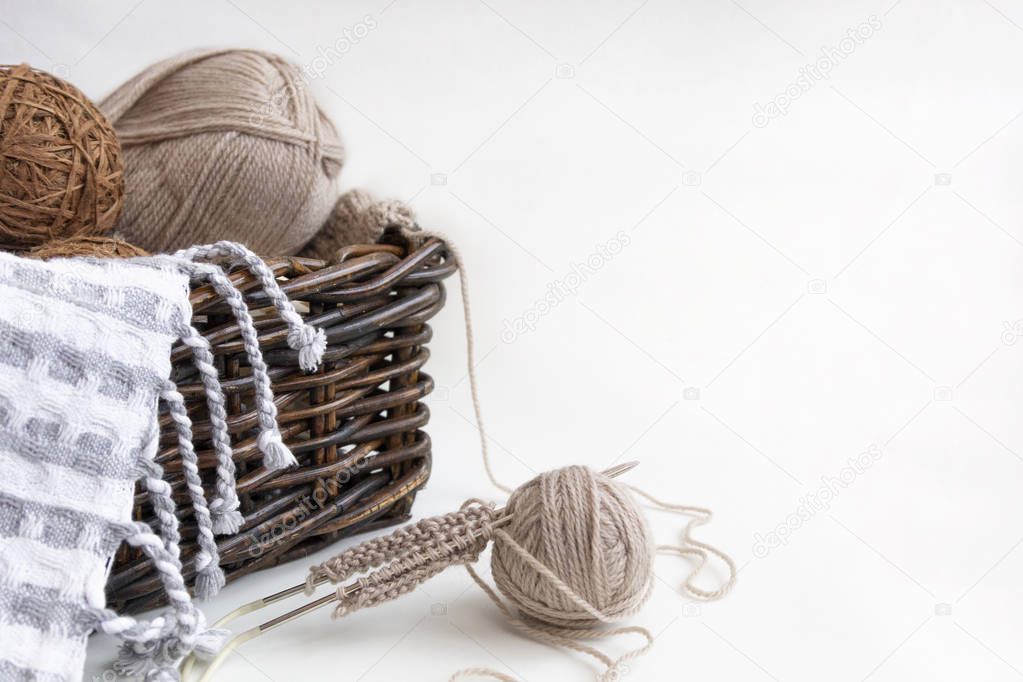 Knitting needles and balls of yarn gray and brown wool yarn in wicker basket on light background. Concept of hobby, handicraft and comfort