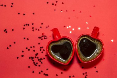 Kırmızı arka planda kalp şeklinde, pırıl pırıl kalpleri olan kırmızı kahve fincanları. Sevgililer Günü konsepti, aşk ve romantizmin sembolü. Üst görünüm, düz görünüm, kopyalama alanı