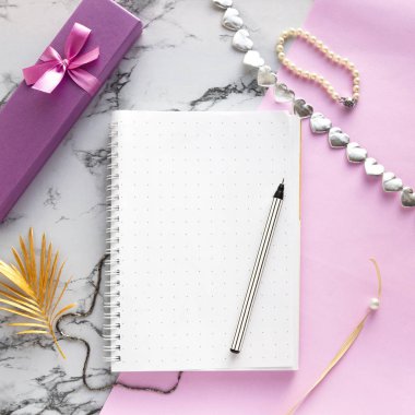 Kadın aksesuar masası. İçinde kalem, hediye, mücevher, bilezik, pembe mermer arka planda altın palmiye yaprağı olan defter. Güzellik blogcuları için çalışma masası. Düz konum, üst görünüm, kopyalama alanı