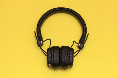Sarı arka planda kablosuz siyah kulaklık. Yaratıcı geçmişe dönük tasarımlardaki modaya uygun aksesuarlar. Müzik hipster konsepti asgari düzeyde. Düz konum, üst görünüm, kopyalama alanı