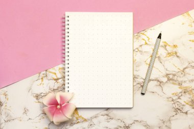 Kadın aksesuar masası - kalemli defter, pembe mermer arka planda çiçek. Güzellik blogcuları için çalışma masası. Düz konum, üst görünüm, kopyalama alanı