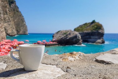 Güzel deniz manzarasının arka planında bir fincan kahve, açık mavi mavi deniz, sahil ve ufuk çizgisi, Karadağ