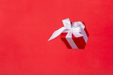Kırmızı arka planda uçan beyaz saten kurdeleli kırmızı hediye kutusu. Noel tatili, doğum günü, sevgililer günü, alışveriş ve satış için en düşük konsept.