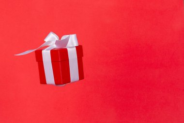 Kırmızı arka planda uçan beyaz saten kurdeleli kırmızı hediye kutusu. Noel tatili, doğum günü, sevgililer günü, alışveriş ve satış için en düşük konsept.