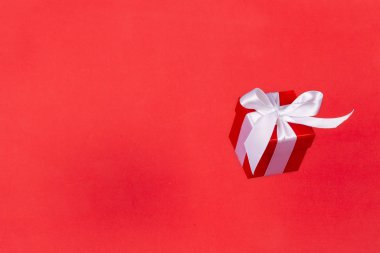 Kırmızı arka planda uçan beyaz saten kurdeleli kırmızı hediye kutusu. Noel tatili, doğum günü, sevgililer günü, alışveriş ve satış için en düşük konsept.