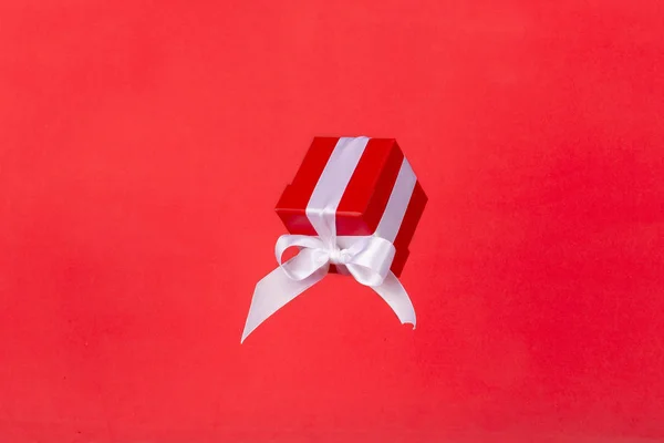 赤い背景に白いサテンリボン弓飛んで赤いギフトボックス クリスマス休暇 誕生日 バレンタイン ショッピング 販売のための最小限の概念 — ストック写真