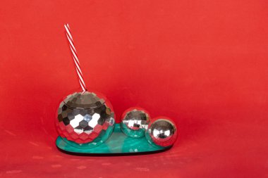 Yaratıcı disko kokteyli şekilli top bardağı ve saman, kırmızı arka planda ışıltılı ve ışıltılı süs köpükleri. Noel tatili ve partiler için kavram.