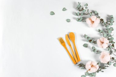 Doğal çevre dostu bambu çatal bıçak seti, okaliptüs yaprakları ve açık mavi arka planda pamuk çiçekleri. Sıfır atık, plastiksiz konsept. Düz konum, üst görünüm, kopyalama alanı