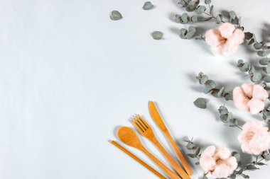 Eko doğal ahşap kaşık, çatal, içmek için bıçak pipetleri, okaliptüs yaprakları ve pastel mavi arka planda pamuk çiçekleri. Sıfır atık, plastiksiz konsept. Düz konum, üst görünüm, kopyalama alanı