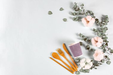 Eko doğal ahşap kaşık, çatal, bıçak, kağıt bardak, okaliptüs yaprakları ve pastel mavi arka planda pamuk çiçekleri. Sıfır atık, plastiksiz konsept. Düz konum, üst görünüm, kopyalama alanı