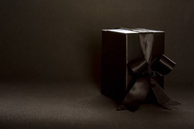 Black gift box with black ribbon bow on dark background, copy space. Valentine's day, birthday romantic concept, greeting card.
