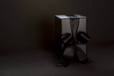 Black gift box with black ribbon bow on dark background, copy space. Valentine's day, birthday romantic concept, greeting card.