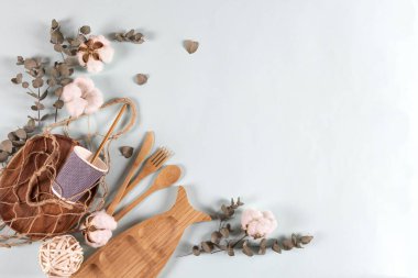 Çevreye özgü ahşap bambu çatal bıçak seti, tel torba örgü, okaliptüs yaprakları ve pastel mavi arka planda pamuk çiçekleri. Sıfır atık, plastiksiz konsept. Düz konum, üst görünüm, kopyalama alanı