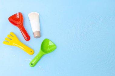 Güneş kremi, çocukların cildine güneş kremi sürerken mavi su yüzeyi üzerinde renkli su oyuncakları, üst manzara. Ultraviyole koruma ürünü kavramı, yaz çocukları kozmetik ürünleri.