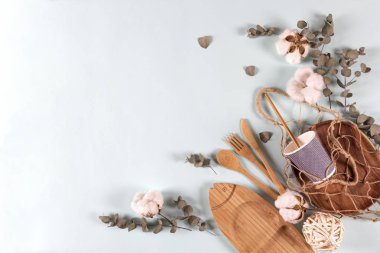 Çevreye özgü ahşap kaşık, çatal, bıçak, tabak, ip torbası ağı, okaliptüs yaprakları ve arka planda pamuk çiçekleri, afiş. Sıfır atık, plastiksiz konsept. Düz konum, üst görünüm, kopyalama alanı