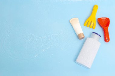Güneş kremi, çocukların cildine güneş kremi sürerken mavi su yüzeyi üzerinde renkli su oyuncakları, üst manzara. Ultraviyole koruma ürünü kavramı, yaz çocukları kozmetik ürünleri.