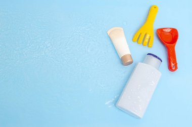 Güneş kremi, çocukların cildine güneş kremi sürerken mavi su yüzeyi üzerinde renkli su oyuncakları, üst manzara. Ultraviyole koruma ürünü kavramı, yaz çocukları kozmetik ürünleri.