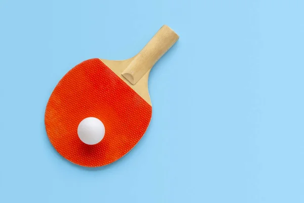 Red racket for table tennis with white ball on blue background. Ping pong sports equipment in minimal style. Flat lay, top view, copy space