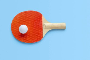 Masa tenisi için kırmızı raket, mavi arka planda beyaz top. Masa tenisi spor ekipmanları minimum düzeyde. Düz konum, üst görünüm, kopyalama alanı