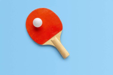 Masa tenisi için kırmızı raket, mavi arka planda beyaz top. Masa tenisi spor ekipmanları minimum düzeyde. Düz konum, üst görünüm, kopyalama alanı