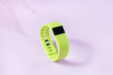 Açık pembe arka planda akıllı takip cihazı. Eğrelti otu gölgesi ve spor bileziği olan yeşil fitness saati.