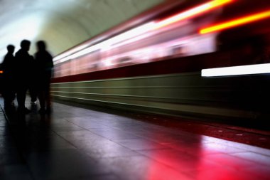 Tren gelirken perondaki yolcuların silueti. Hareket halindeki trenin bulanık görüntüsü ve platformdaki insanların siluetleri.