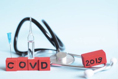 Üzerinde COVD metni olan kırmızı küpler, steteskop ve mavi arka planda ampul. Koronavirüs konseptini yenmek.