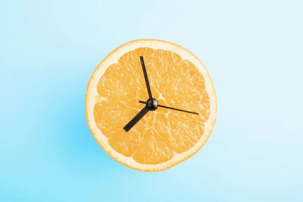 Fresh orange with clock arrows. Healthy nutrition/healthy lifestyle concept on blue background.