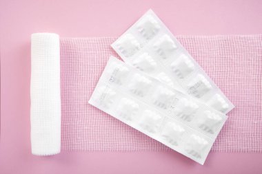 Pembe arka planda steril gazlı bez ve ilaçlar..