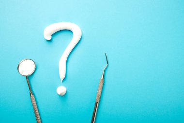 Diş aletleri ve mavi arkaplanda beyaz bir diş macunu soru işareti.