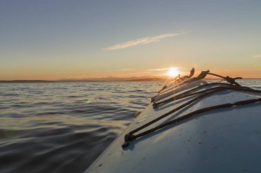 Nose of kayak at sea pointed toward the setting sun.