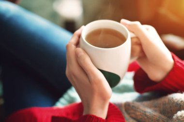 Güzel kadının el kırmızı kazaklı çay sabah güneş ışığı altında tutarak yakın çekim.