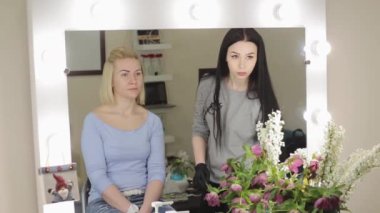 Makyöz ve modeli. Genç kadın. Güzel bir kız bir güzellik salonu bir ayna önünde profesyonel bir fırça ile kaşları çizim makyaj sanatçısı.