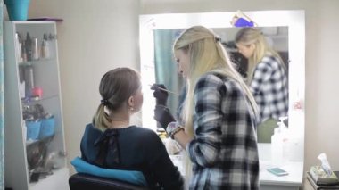 Makyöz ve modeli. Genç sarışın. Güzel bir kız bir güzellik salonu bir ayna önünde profesyonel bir fırça ile kaşları çizim makyaj sanatçısı.