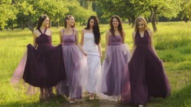 Güzel gelin ve bridemaids mor elbiseler park veya Bahçe el ele tutuşarak ve akşamları gülüyor yürüyüş.