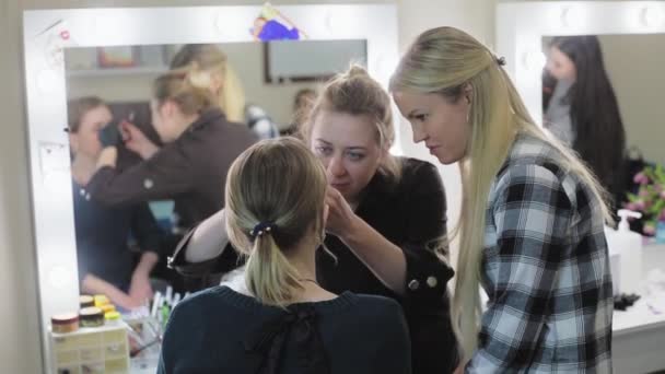 Make-up artist, student and model. The learning process. Young blonde. The make-up artist drawing eyebrows to a pretty girl with a professional brush in front of a mirror in a beauty salon. — Stock Video