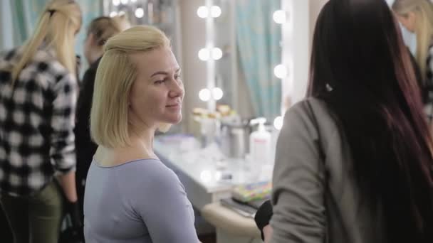 Maquiagem artista e modelo. Jovem. A maquilhadora desenhando sobrancelhas para uma garota bonita com um pincel profissional na frente de um espelho em um salão de beleza . — Vídeo de Stock