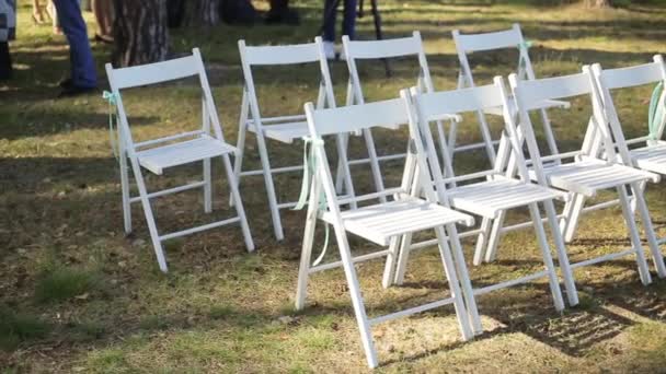 Bröllop setup i trädgård, park. Utanför bröllop, fest. Bröllop mittgång inredning. Rader av vita trä tomma stolar på gräsmattan innan vigseln. Långsam pan. — Stockvideo