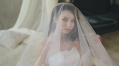 Nazik bir çekici esmer sabah. Güzel gelin gülümseyen ve yatakta otururken peçe dokunmadan pencere bakarak.