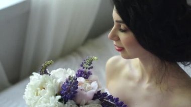 Nazik bir çekici esmer sabah. Güzel gelin gülümseyen ve yatakta otururken pencere ve bir buket arıyorsunuz.